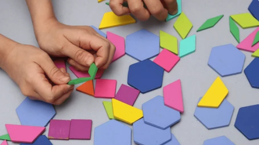 Hands assembling bright color geometric shapes (hexagons and triangles) on a light surface 